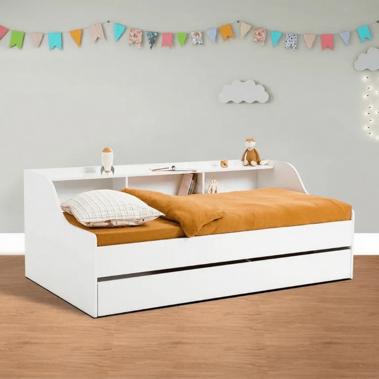 A child's white daybed with a built-in bookshelf headboard and two pull-out storage drawers.