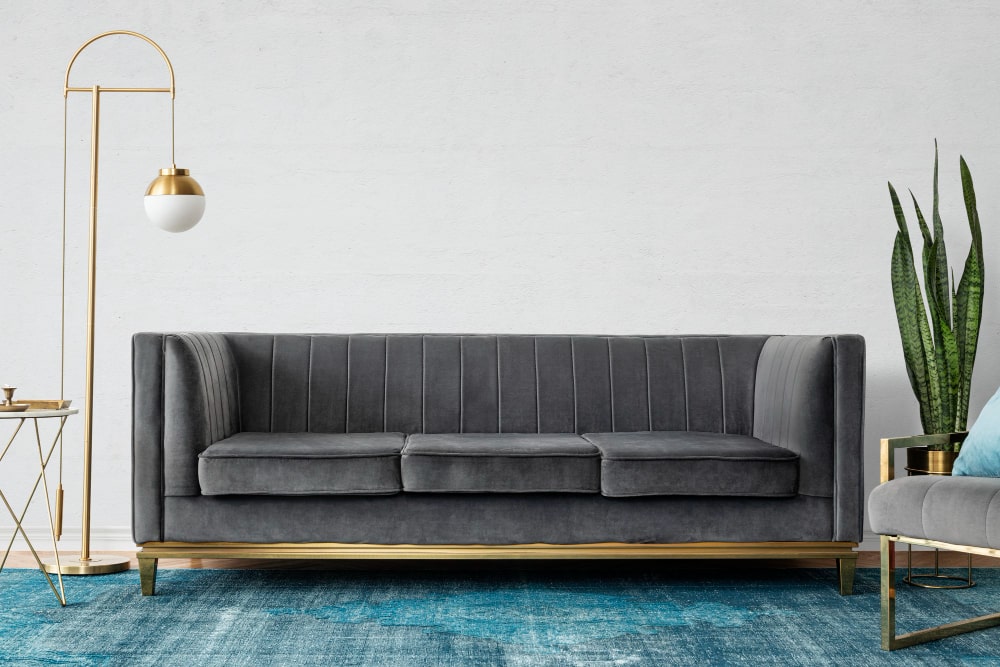 Luxurious dark gray velvet sofa with chic fluted arms and a gleaming gold base, exuding modern elegance.